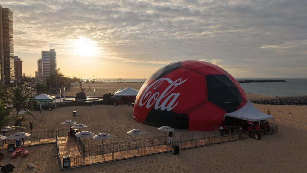 Coca-Cola Fanzone leva domo imersivo gratuito à Praia de Iracema entre 24 e 27 de junho, com DJs, simuladores de gol e projeto de reciclagem na Copa 2026.