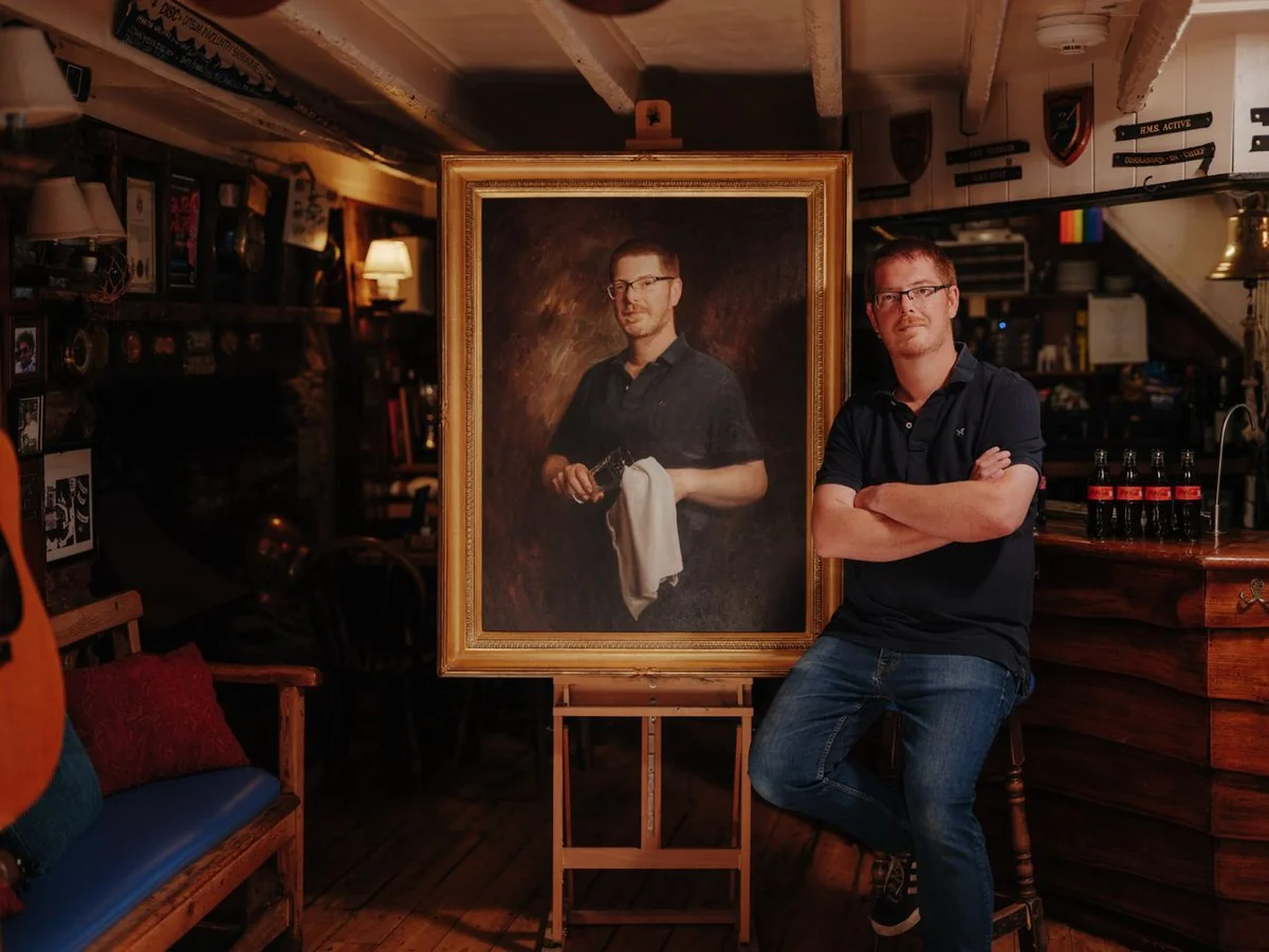 Simon Dafforn-Jones ao lado do seu retrato no pub Ferry Boat Inn, em Dittisham